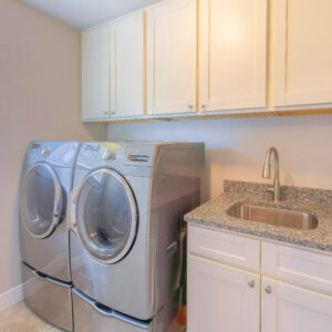Square Laundry interior with front load laundry units and vanity sink. Laundry room with window near the washing machines below the top wall cabinets.